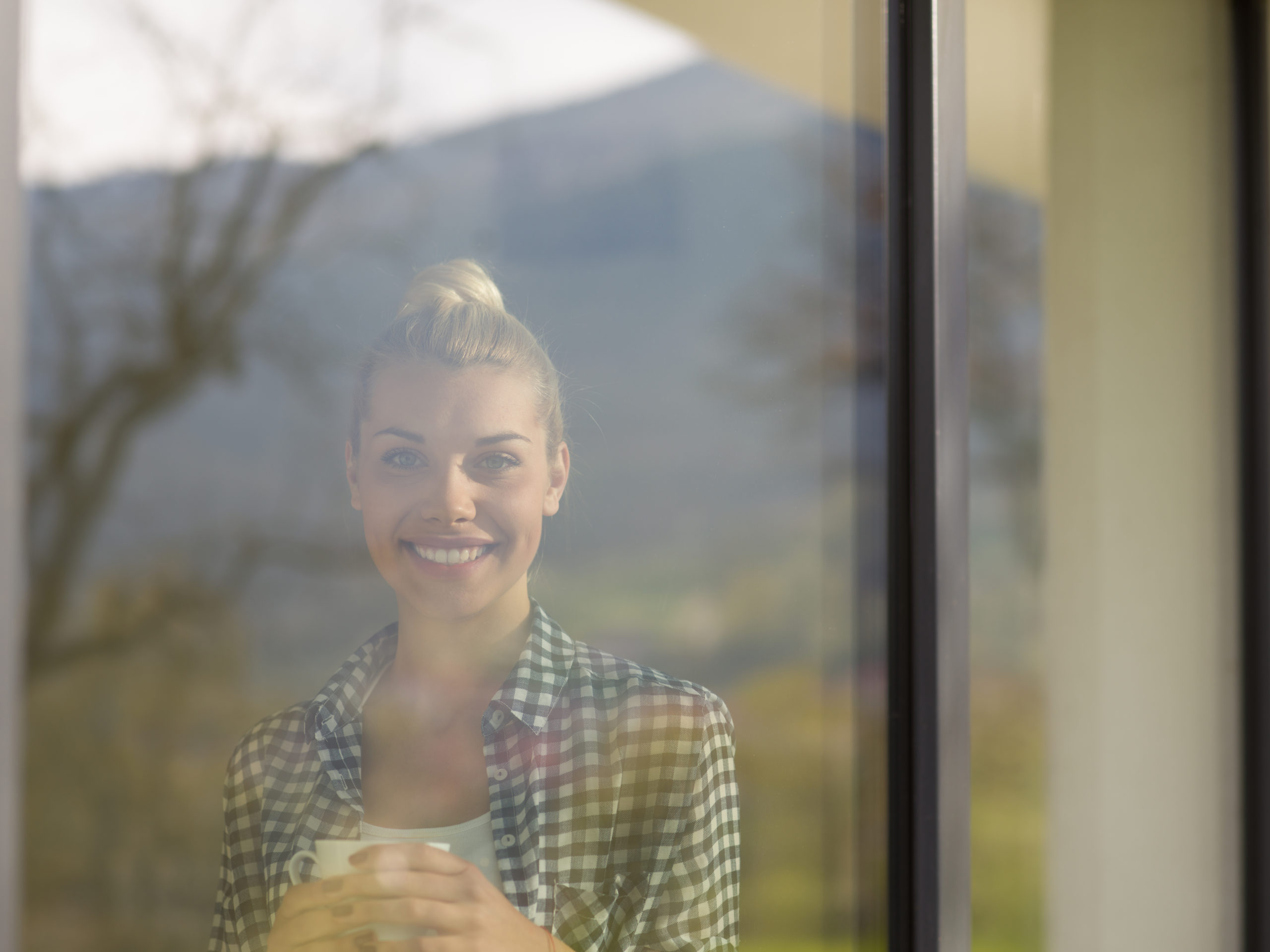 young woman drinking morning coffee by the window to illustrate best home window tinting and sun blocking window film