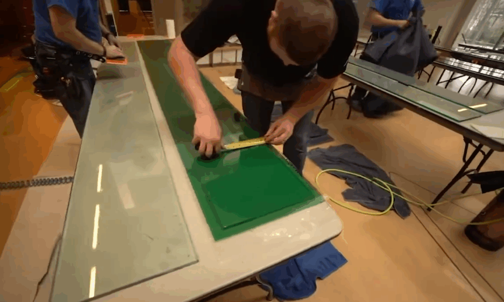 A crewmember adding green film to a pane of glass on a table.