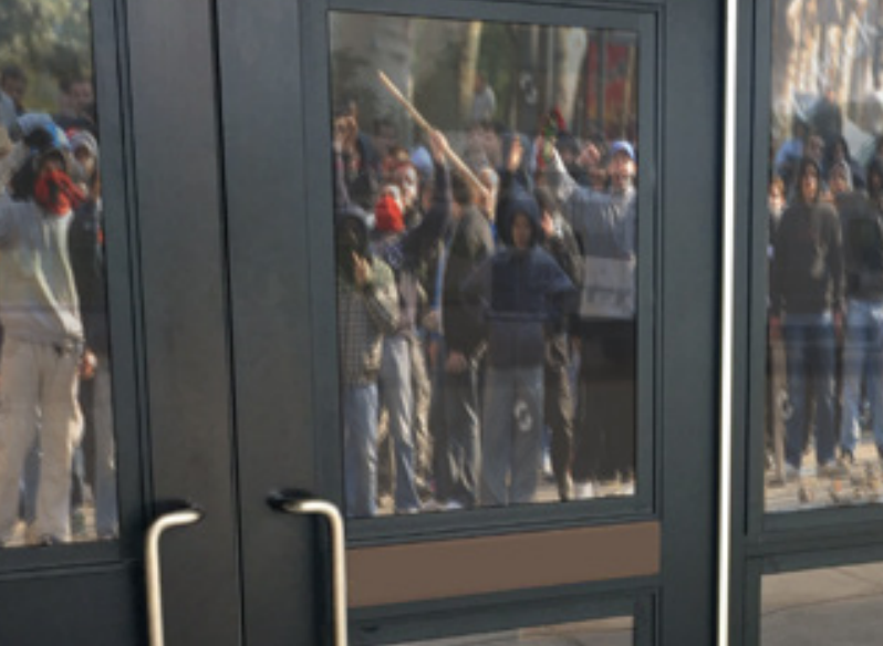 A gathering crowd reflected in a glass door to illustrate DefenseLite Security SHields