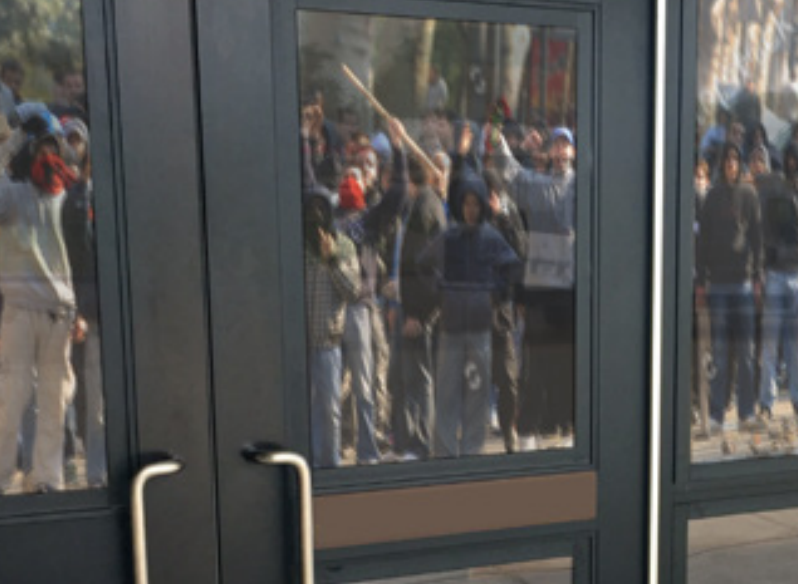 A gathering crowd reflected in a glass door to illustrate DefenseLite window film.
