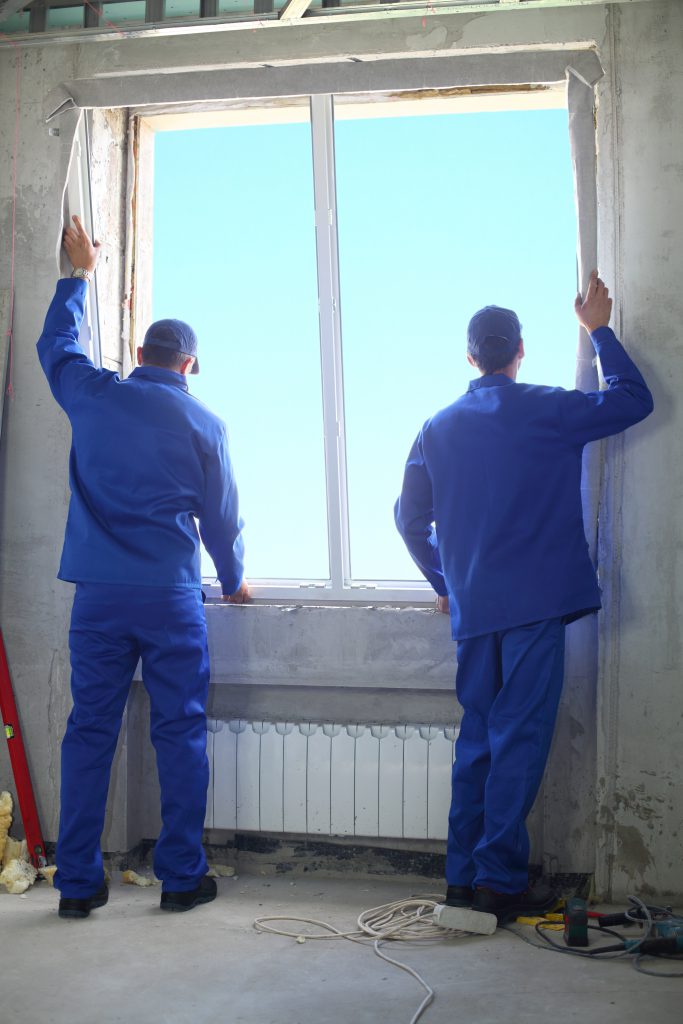 Two men in working clothes set new window frame