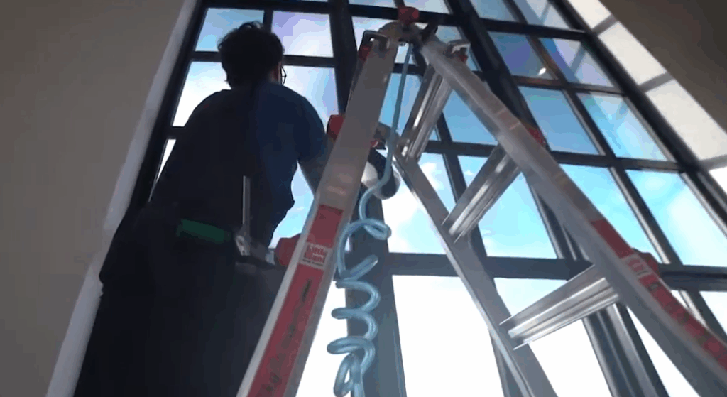 A ctrewmember on a ladder applying film to a very large bank of windows