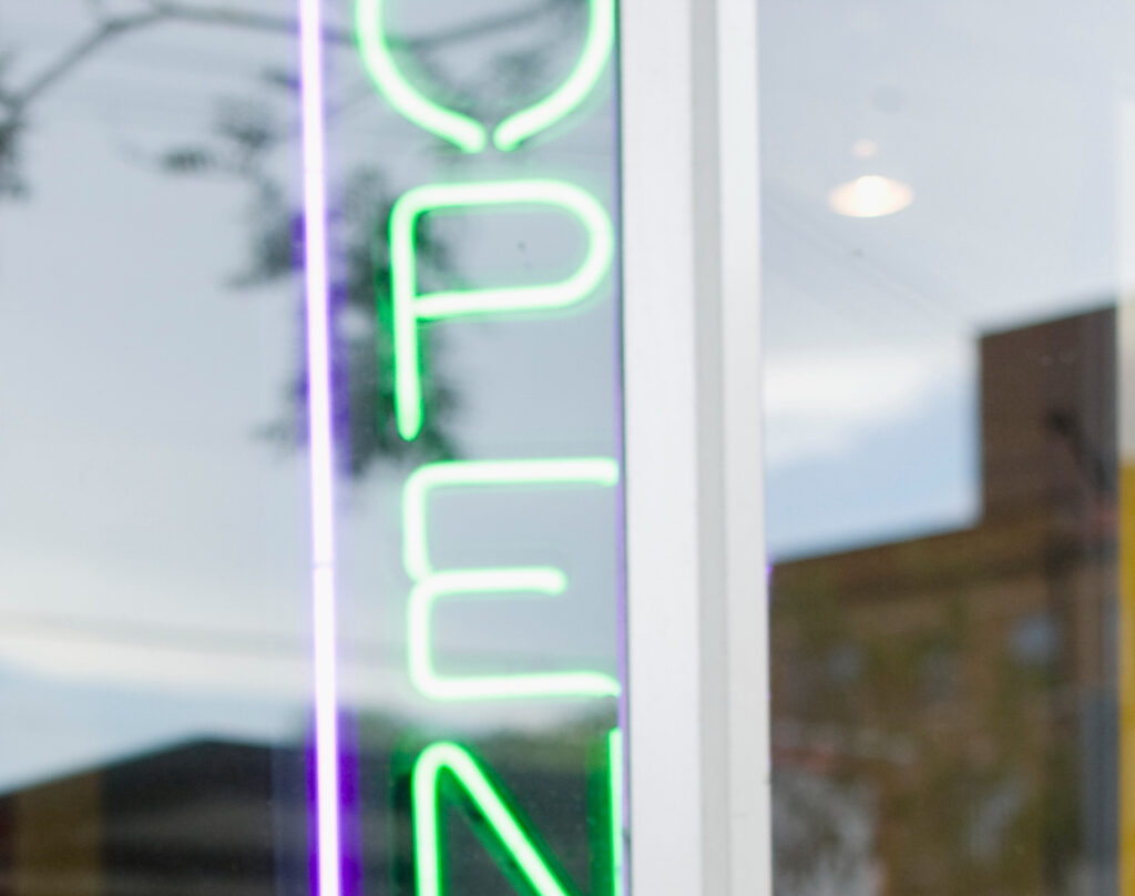 Closeup of storefront window with verticle neon open sign to illustrate Storefront Window Protection