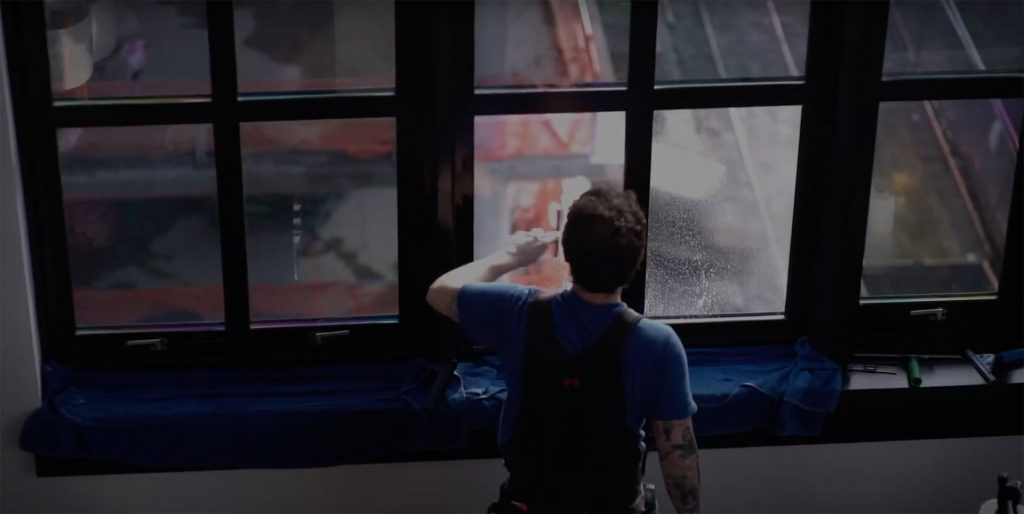 Team member cleaning a window in a bright, urban office setting.